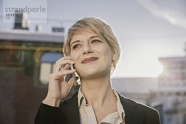 Porträt der lächelnden blonden Geschäftsfrau am Telefon bei Gegenlicht