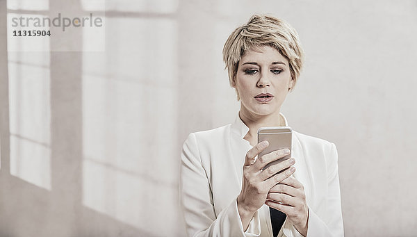 Porträt einer blonden Geschäftsfrau beim Blick aufs Handy