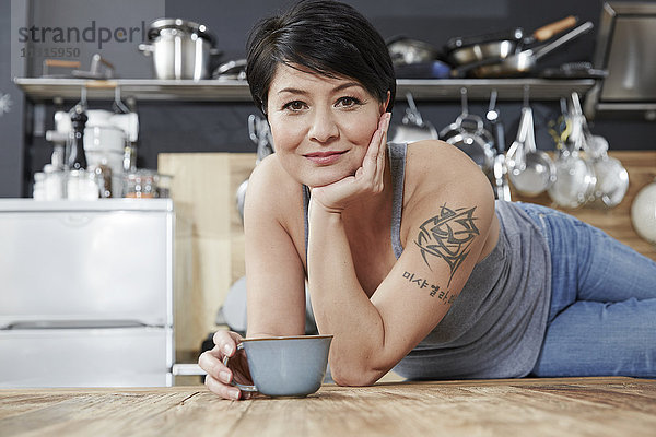 Porträt der lächelnden Frau in der Küche mit Tasse Kaffee
