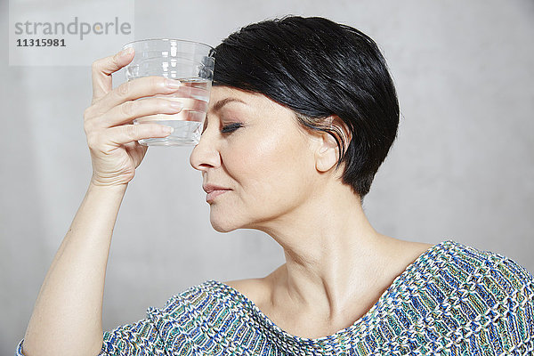 Frau hält sich ein Glas Wasser an die Stirn