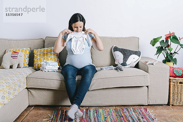 Schwangere Frau sitzt auf der Couch und schaut auf Babyschläfer.