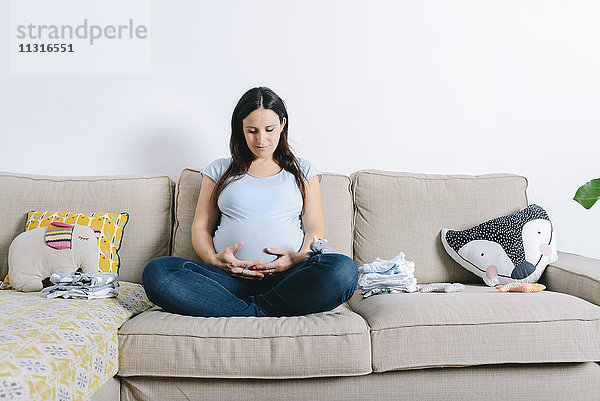 Schwangere Frau sitzt auf der Couch und hält den Bauch.