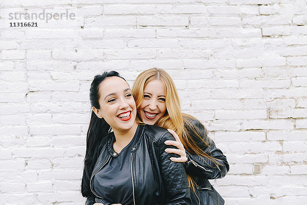Zwei lachende junge Frauen vor weißer Ziegelwand