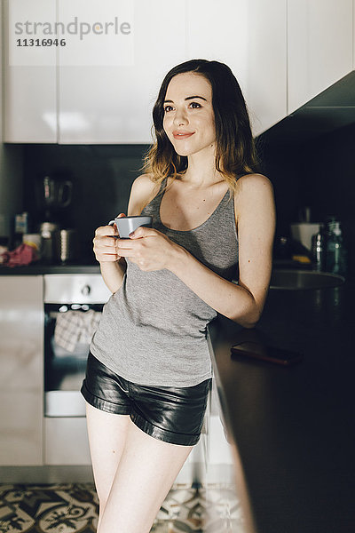 Lächelnde junge Frau beim Kaffeetrinken in der Küche