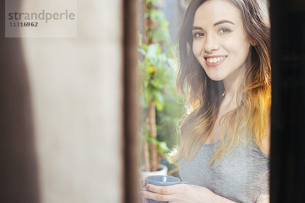 Porträt einer lächelnden jungen Frau beim Kaffeetrinken