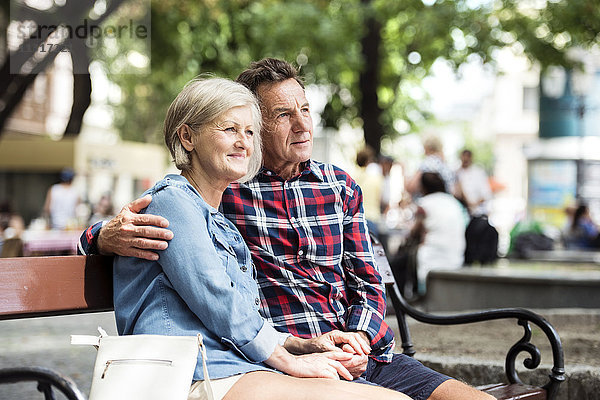 Seniorenpaar sitzt auf der Bank und schaut sich etwas an.
