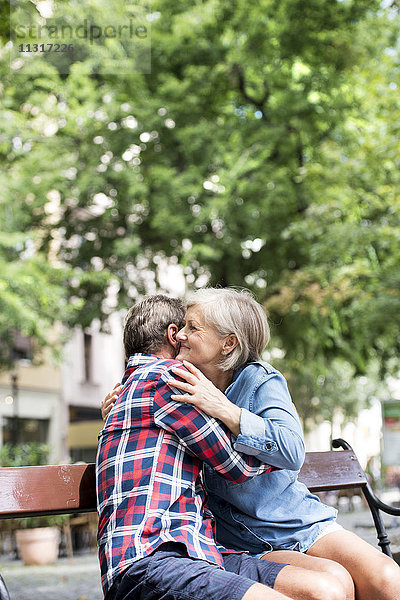 Fröhliches Seniorenpaar  das sich auf einer Bank umarmt.