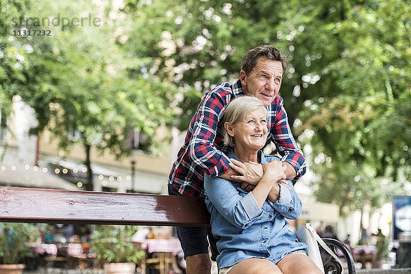 Älterer Mann  der seine Frau auf einer Bank umarmt.