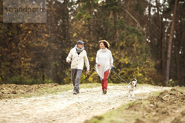 Seniorenpaar  das mit ihrem Hund im Wald spazieren geht.