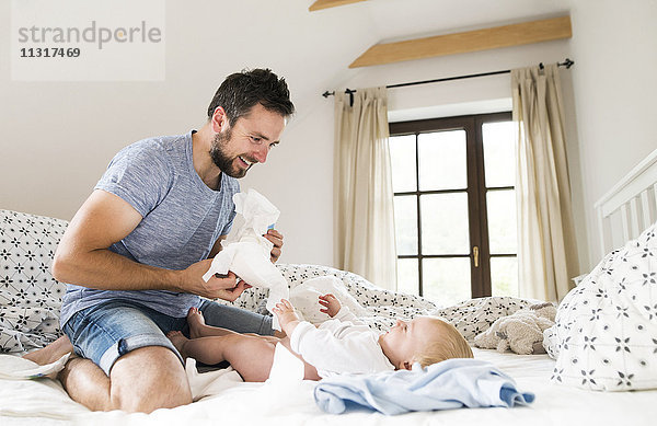 Vater wickelt Babywindeln auf dem Bett.