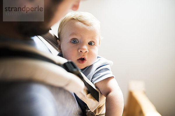 Glücklicher Vater mit Baby im Tragesitz zu Hause