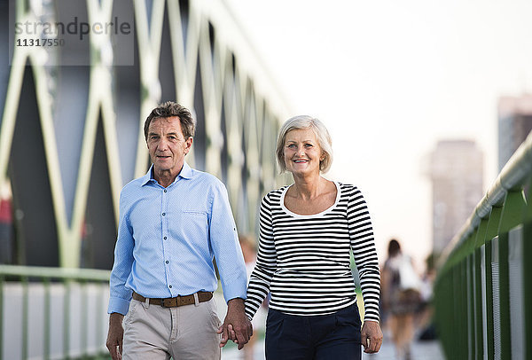 Seniorenpaar  das Hand in Hand auf einer Brücke geht.