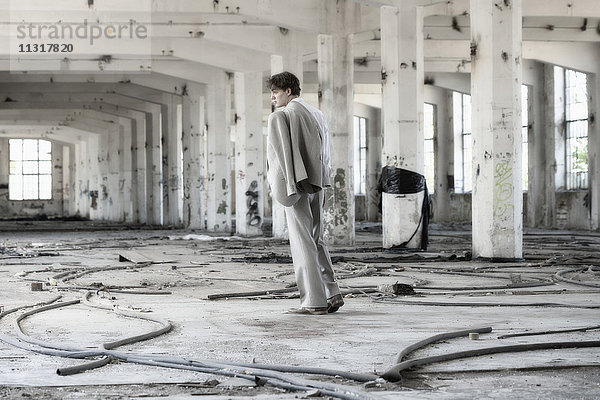 Junger Mann im Anzug vor einem verlassenen Gebäude.