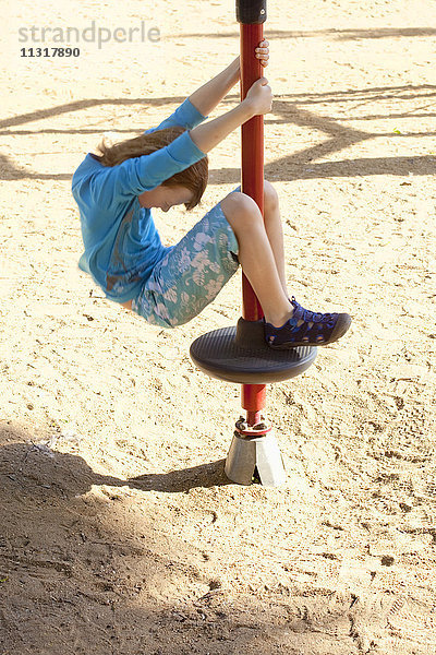 Junge mit blondem Haar  der sich auf dem Spielplatz an einer Stange dreht