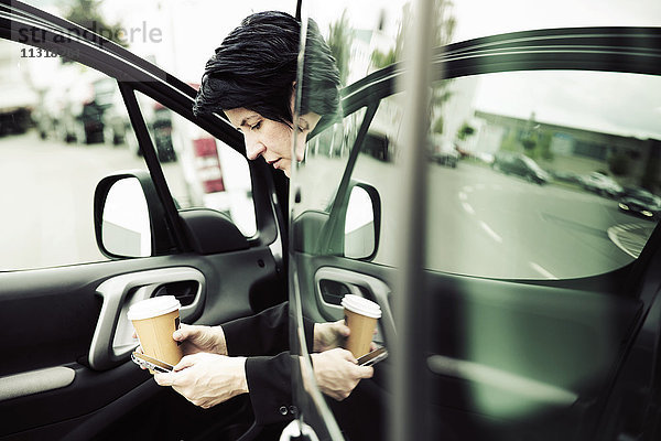 Geschäftsfrau im Auto sitzend  mit Smartphone