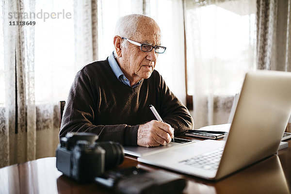 Senior-Fotograf bei der Arbeit mit dem Laptop zu Hause