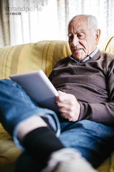 Älterer Mann auf der Couch sitzend mit Tablette
