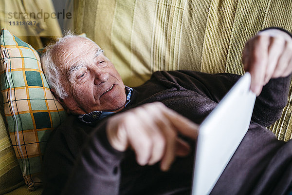 Senior auf der Couch liegend mit Tablette