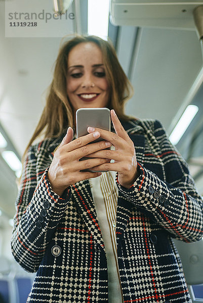 Lächelnde Frau im Zug beim Blick aufs Handy