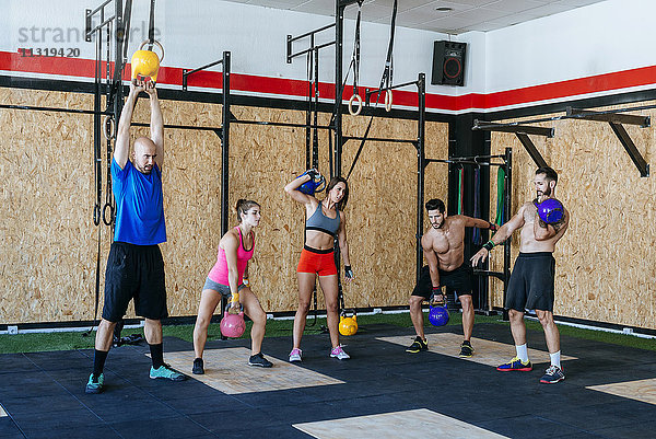 Gruppe von Sportlern beim Heben von Kettlebells im Fitnessstudio