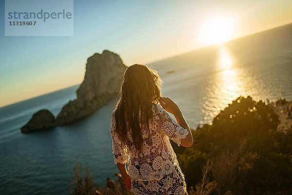Spanien  Ibiza  Frau mit Blick auf das Meer und die Insel Es Vedra bei Sonnenuntergang