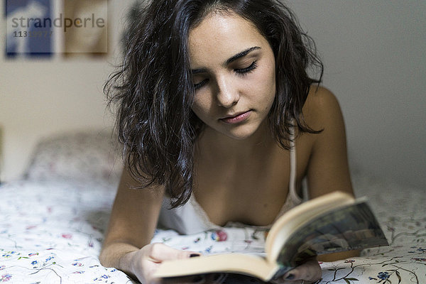 Junge Frau liegt auf dem Bett und liest ein Buch.