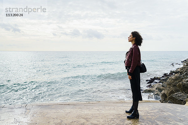 Frau steht vor dem Meer und schaut in die Ferne.