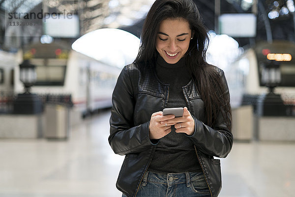 Glückliche junge Frau mit Handy am Bahnhof