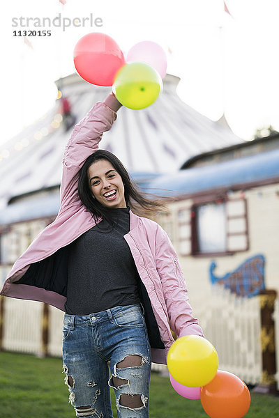 Glückliche junge Frau hält Luftballons im Freien.