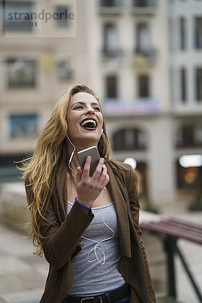 Glückliche junge Frau beim Musikhören mit Kopfhörer und Smartphone