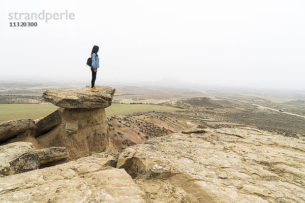 Spanien  Navarra  Bardenas Reales  junge Frau steht auf einem Felsen im Naturpark und schaut sich um