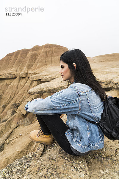 Spanien  Navarra  Bardenas Reales  junge Frau auf einem Felsen im Naturpark sitzend  mit Blick auf die Aussicht