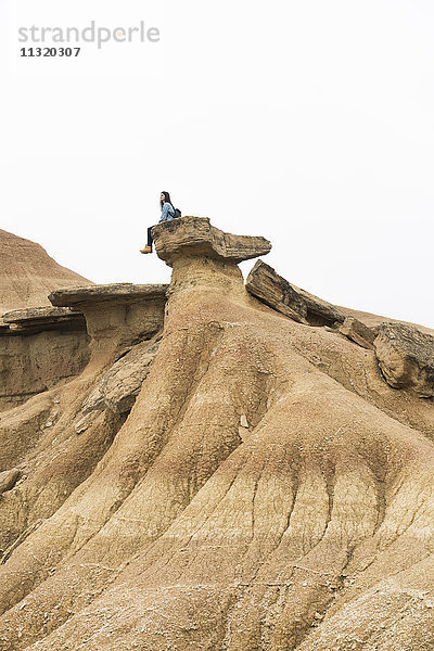 Spanien  Navarra  Bardenas Reales  junge Frau auf einem Felsen im Naturpark sitzend  mit Blick auf die Aussicht