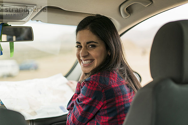 Porträt der lachenden jungen Frau mit Karte im Auto