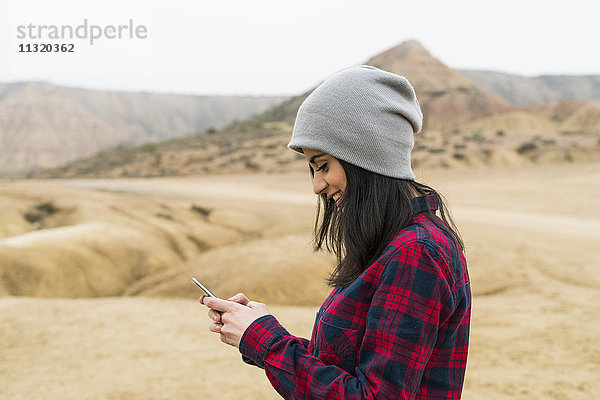 Spanien  Navarra  Bardenas Reales  lächelnde junge Frau beim Blick aufs Handy im Naturpark