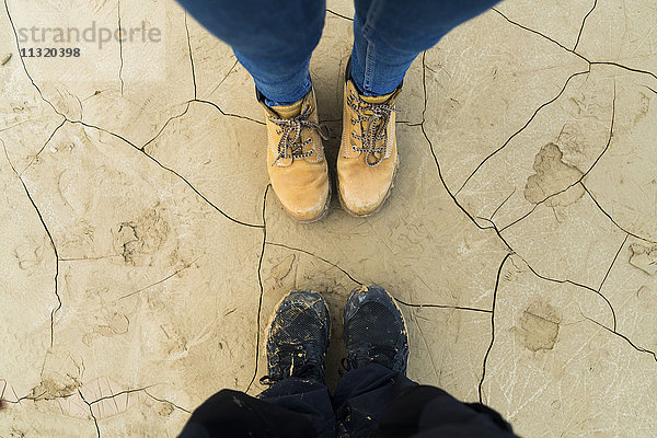 Füße eines Paares  das auf getrocknetem  rissigen Boden steht.