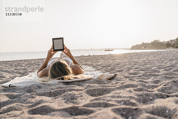 Junge Frau auf der Decke am Strand liegend mit Tablette