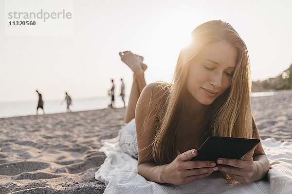 Junge Frau auf der Decke am Strand liegend mit Tablette