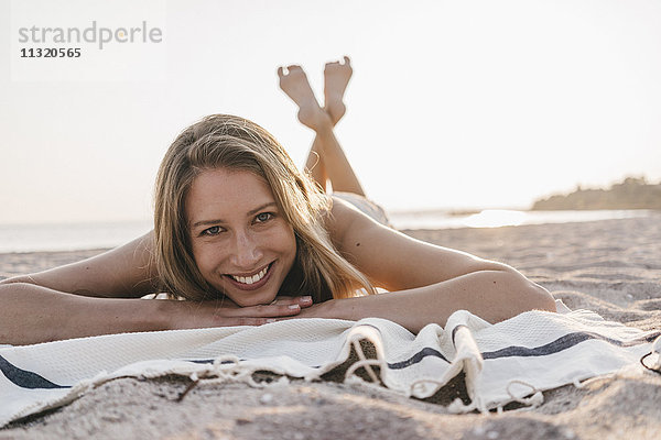 Fröhliche junge Frau auf der Decke am Strand liegend