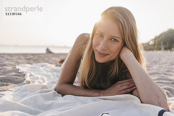 Porträt einer jungen Frau  die auf einer Decke am Strand liegt.