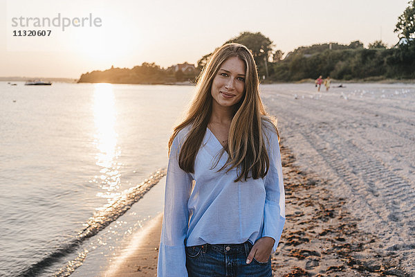 Lächelnde junge Frau am Strand bei Dämmerung