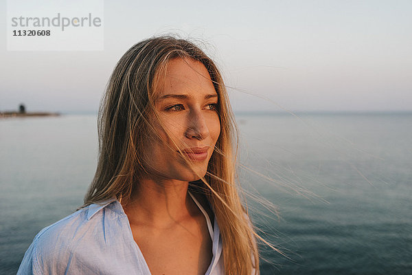 Porträt einer jungen Frau vor dem Meer bei Sonnenuntergang