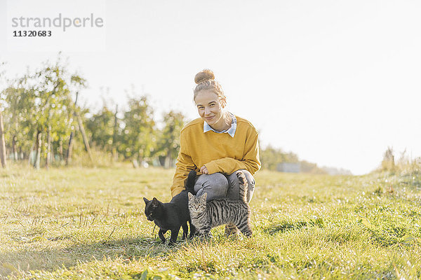 Lächelnde junge Frau mit zwei Katzen auf dem Land