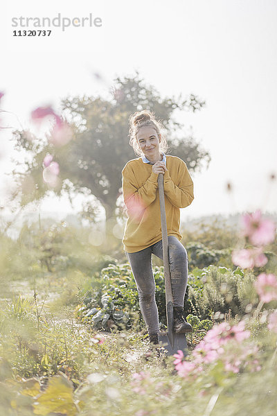Lächelnde junge Frau mit Spaten im Bauerngarten