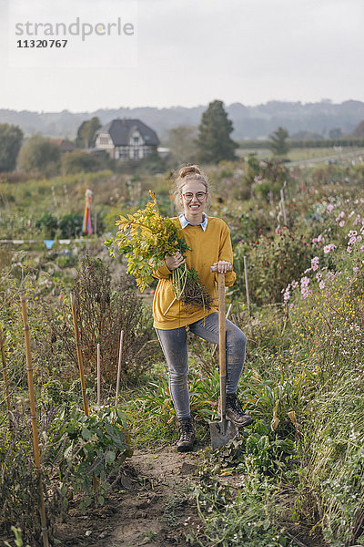 Lächelnde junge Frau hält Pflanze im Bauerngarten