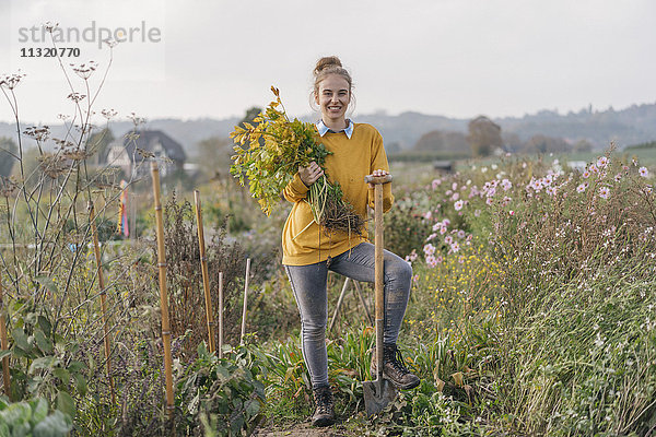 Lächelnde junge Frau hält Pflanze im Bauerngarten