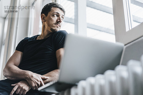 Mann auf Heizung sitzend mit Laptop