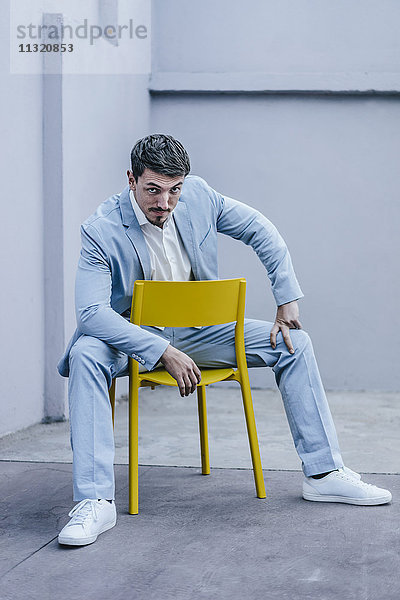 Porträt eines selbstbewussten Geschäftsmannes auf gelbem Stuhl