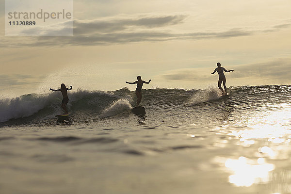 Indonesien  Bali  drei Surfer bei Sonnenuntergang