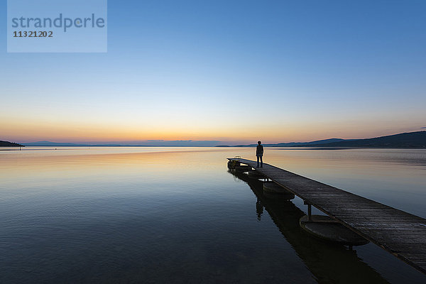Italien  Umbrien  Trasimeno-See  Silhouette des Mannes  der am Steg steht und den Sonnenuntergang beobachtet.